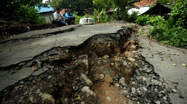 Dua warga duduk di dekat jalan desa yang terbelah akibat bencana tanah bergerak di Desa Dermasuci, Kabupaten Tegal, Jawa Tengah, Senin (14/2/2022).  ANTARA FOTO/Oky Lukmansyah