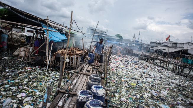 Warga memikul jeriken air melintasi jembatan kayu di antara sampah di kawasan perkampungan nelayan Cilincing, Jakarta Utara, Minggu (20/2/2022). [ANTARA FOTO/Aprillio Akbar/tom]