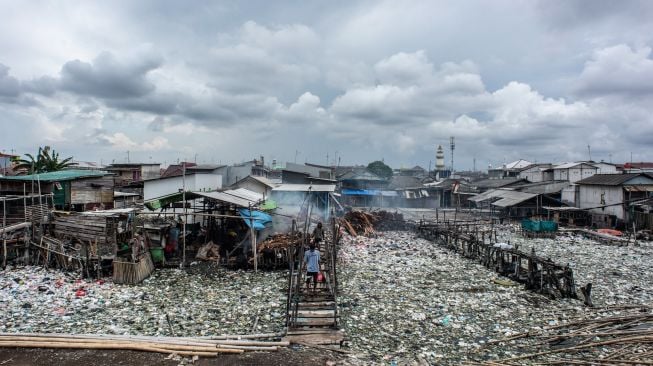 Warga berjalan di antara sampah di kawasan perkampungan nelayan Cilincing, Jakarta Utara, Minggu (20/2/2022). [ANTARA FOTO/Aprillio Akbar/tom]