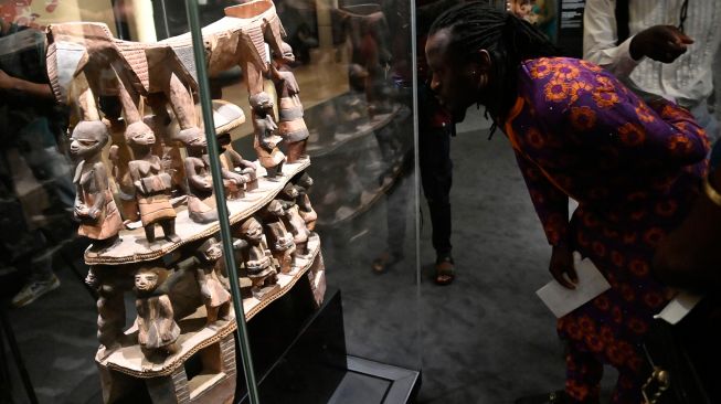 Pengunjung melihat artefak peninggalan kota suci Kana saat pameran artefak Benin yang dijarah dan pameran karya seni kontemporer yang digelar di kantor kepresidenan di Cotonou, Benin, Jumat (18/2/2022). [PIUS UTOMI EKPEI/AFP] 
