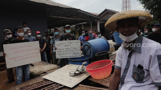 Sejumlah perajin tempe melakukan aksi unjuk rasa di kawasan Sentra Produksi Tempe, Cimanggis, Depok, Jawa Barat, Senin (21/2/2022). [Suara.com/Angga Budhiyanto]