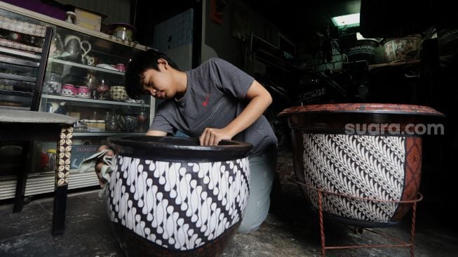 Andika Dwi Pangga (16) menyelesaikan pembuatan batik rekat pada media pot bunga di Say Galery, Sukmajaya, Depok, Jawa Barat, Senin (21/2/2021). [Suara.com/Angga Budhiyanto]