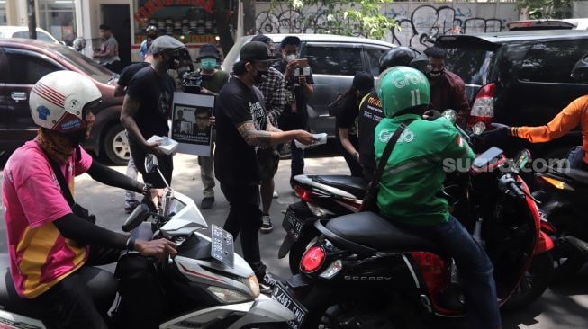 Penggemar musisi Jerinx SID dan band Superman Is Dead (SID), Outsider membagikan makanan dan masker kepada pengendara yang melintas saat menggelar aksi solidaritas di depan Pengadilan Negeri (PN) Jakarta Pusat, Jakarta, Selasa (22/2/2022). [Suara.com/Angga Budhiyanto]