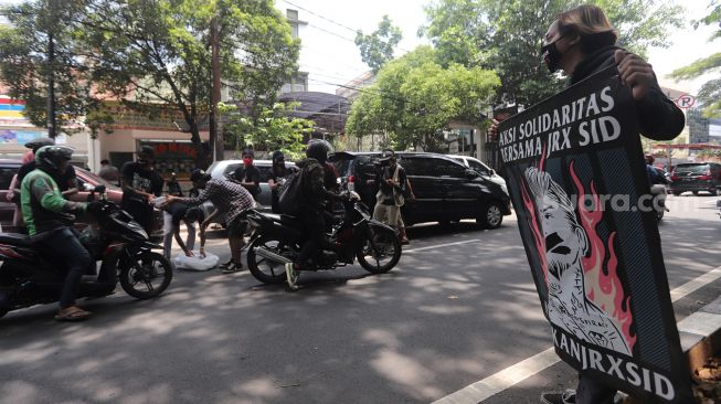 Penggemar musisi Jerinx SID dan band Superman Is Dead (SID), Outsider membagikan makanan dan masker kepada pengendara yang melintas saat menggelar aksi solidaritas di depan Pengadilan Negeri (PN) Jakarta Pusat, Jakarta, Selasa (22/2/2022). [Suara.com/Angga Budhiyanto]