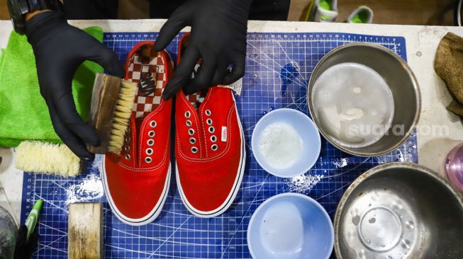 Kru membersihkan sepatu pelanggan di Cleaning Shoes Kicks Kemon, Haji Nawi, Jakarta Selatan, Rabu (23/2/2022). [Suara.com/Alfian Winanto]