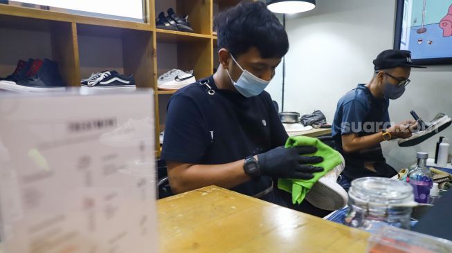 Kru membersihkan sepatu pelanggan di Cleaning Shoes Kicks Kemon, Haji Nawi, Jakarta Selatan, Rabu (23/2/2022). [Suara.com/Alfian Winanto]