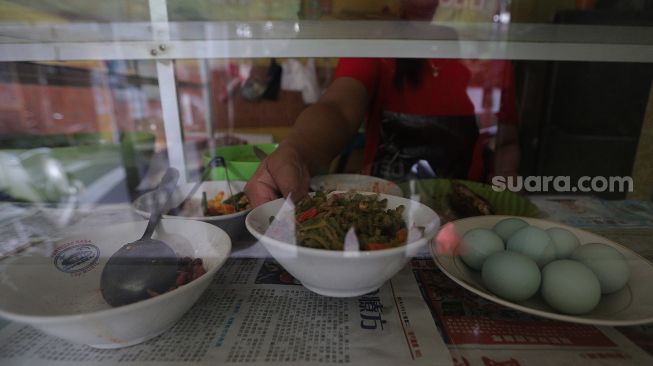 Penjual menata lauk pauk di salah satu warung di kawasan Jati Padang, Pasar Minggu, Jakarta, Rabu (23/2/2022). [Suara.com/Angga Budhiyanto] 