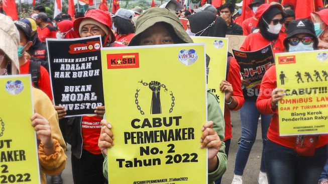 Massa buruh membawa poster dan spanduk berisi tuntutan saat menggelar aksi unjuk rasa di depan gedung Kementerian Tenaga Kerja (Kemenaker) di Setia Budi, Jakarta Selatan, Rabu (23/2/2022). [Suara.com/Alfian Winanto]