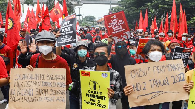 Massa buruh membawa poster dan spanduk berisi tuntutan saat menggelar aksi unjuk rasa di depan gedung Kementerian Tenaga Kerja (Kemenaker) di Setia Budi, Jakarta Selatan, Rabu (23/2/2022). [Suara.com/Alfian Winanto]