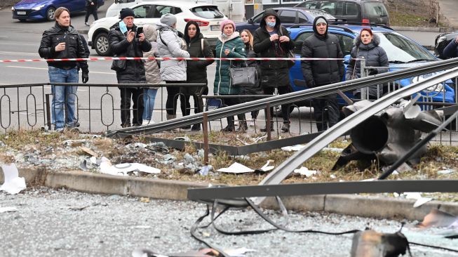 Orang-orang bereaksi berdiri di belakang area tertutup di sekitar sisa-sisa peluru di Kyiv pada 24 Februari 2022. Sergei SUPINSKY / AFP
