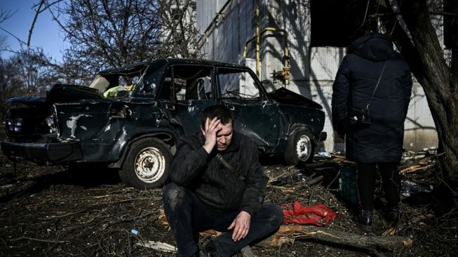 Seorang lelaki di Kota Chuguiv tampak bersedih dengan latar belakang sebuah mobil yang hancur akibat serangan Rusia. (Foto: AFP)