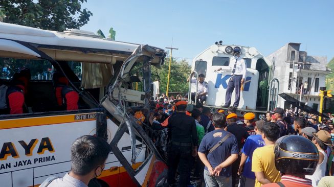 Warga melihat proses evakuasi lokomotif KA Rapih Dhoho yang menabrak bus pariwisata PO Harapan Jaya di perlintasan kereta api tanpa palang pintu di Desa Ketanon, Tulungagung, Jawa Timur, Minggu (27/2/2022). [ANTARA FOTO/Deny Trisdanto//DS/aww]