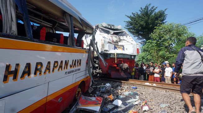 Warga melihat dari dekat kondisi bus dan lokomotif KA Rapih Dhoho yang rusak berat usai tabraka maut di perlintasan kereta api tanpa palang pintu di Desa Ketanon, Tulungagung, Jawa Timur, Minggu (27/2/2022). [ANTARA FOTO/Deny Trisdanto//DS/aww]