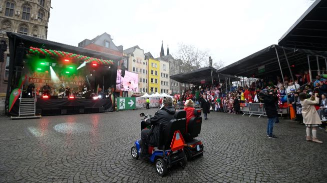 Dua orang di kursi roda listrik duduk melihat pertunjukan di depan panggung  saat acara musim Karnaval di Cologne, Jerman barat, Kamis (24/2/2022). [Ina Fassbender / AFP]