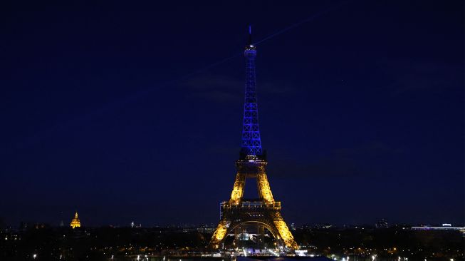 Menara Eiffel menyala dengan warna biru dan kuning yang menggambarkan warna bendera Ukraina di Paris, Prancis, Jumat (25/2/2022). [Thomas COEX / AFP]