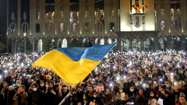 Para pengunjuk rasa memegang ponsel mereka dengan obor yang menyala saat bendera Ukraina dikibarkan selama unjuk rasa mendukung Ukraina di Tbilisi, Georgia, Jumat (25/2/2022). [Vano Shalamov / AFP]