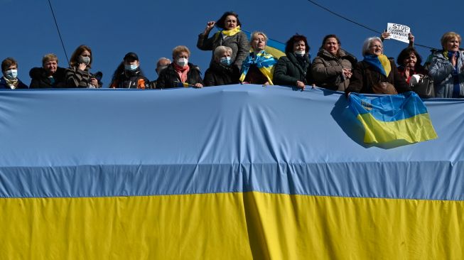 Warga Yunani memegang bendera besar Ukraina saat demonstrasi menentang invasi Rusia ke Ukraina di depan Gedung Parlemen di Athena, Yunani, Minggu (27/2/2022). [Louisa GOULIAMAKI / AFP]
