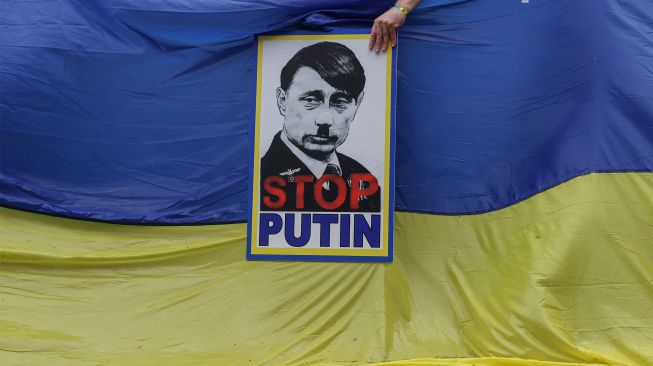 Seorang anggota Asosiasi Ukraina Afrika Selatan memegang poster yang menggambarkan Presiden Rusia Vladimir Putin sebagai Adolf Hitler selama protes mendukung Ukraina di depan Kedutaan Besar Rusia di Pretoria, Afrika Selatan, Jumat (25/2/2022). [Phill Magakoe / AFP]