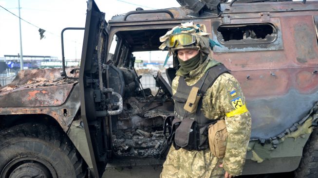 Seorang pejuang Pertahanan Teritorial Ukraina memeriksa kendaraan infanteri Rusia GAZ Tigr yang hancur setelah pertempuran di Kharkiv, Ukraina, Minggu (27/2/2022). [Sergey BOBOK / AFP]  