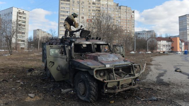 Seorang pejuang Pertahanan Teritorial Ukraina memeriksa kendaraan  infanteri Rusia GAZ Tigr yang hancur setelah pertempuran di Kharkiv, Ukraina, Minggu (27/2/2022). [AFP/Sergey Bobok]. 