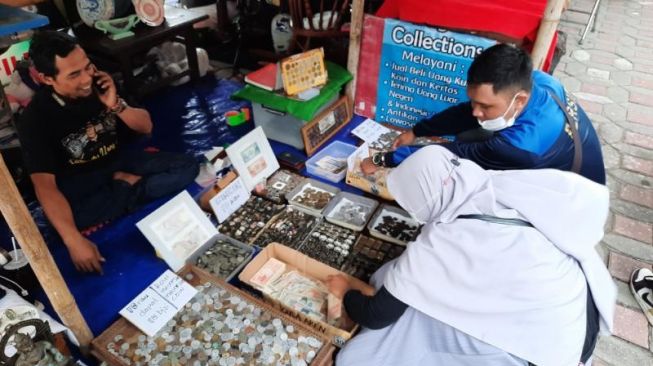 Bagus Manggala (kaus hitam) sedang melayani pembeli koin kuno saat even  Pasar Kangen, Kompleks Kantor Dinas Perpustakaan dan Arsip DIY, Senin (28/2/2022). [Muhammad Ilham Baktora / SuaraJogja.id]