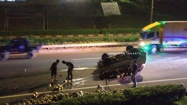 Tangkapan layar video mobil pikap bermuatan kelapa terbalik di Tol JORR arah Pasar Rebo, Jakarta Selatan, Senin (28/2/2022) malam. [Instagram@merekamjakarta]