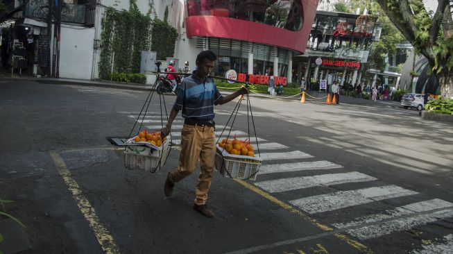 Seorang pedagang buah memikul dagangannya saat berjalan di depan Ciwalk Plaza, Bandung, Jawa Barat, Jumat (4/3/2022). ANTARA FOTO/Novrian Arbi
