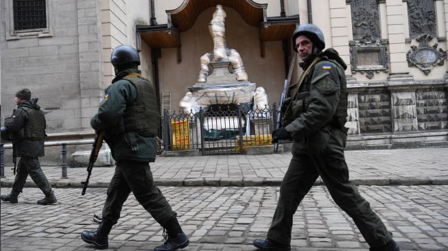 Prajurit Ukraina berjalan melewati patung-patung bersejarah yang dibungkus di Archcathedral Basilica of the Assumption of the Blessed Virgin Mary atau Katedral Latin di Lviv, Ukraina, Sabtu (5/3/2022). [Daniel LEAL / AFP]
