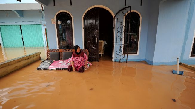 Warga duduk di depan teras rumahnya yang tergenang banjir di Kenali Asam Bawah, Jambi, Minggu (6/3/2022). [ANTARA FOTO/Wahdi Septiawan/foc]