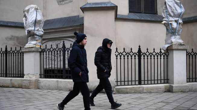 Warga berjalan melewati patung-patung bersejarah yang dibungkus di Archcathedral Basilica of the Assumption of the Blessed Virgin Mary atau Katedral Latin di Lviv, Ukraina, Sabtu (5/3/2022). [Daniel LEAL / AFP] 