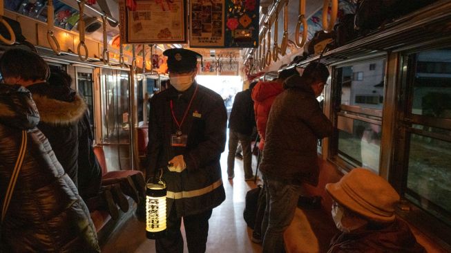 Kondektur membawa lentera saat penumpang menaiki kereta yang populer untuk tur wisata malam hari yang melintasi jalur kereta Gakunan melalui kawasan industri di Fuji, prefektur Shizuoka, Jepang, Sabtu (26/2/2022). [Philip FONG / AFP]
