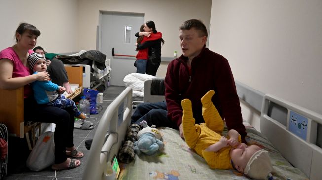 Orang tua dan anak-anak mereka yang merupakan pasien rumah sakit anak pusat Kyiv mengumpulkan barang-barang sebelum dievakuasi ke Polandia dan Jerman di Kyiv, Ukraina, Sabtu (5/3/2022). [Sergei SUPINSKY / AFP]
