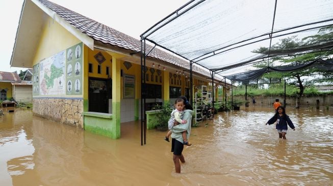 Warga berjalan di halaman sekolah yang tergenang banjir di Kota Baru, Jambi, Minggu (6/3/2022). [ANTARA FOTO/Wahdi Septiawan/foc]