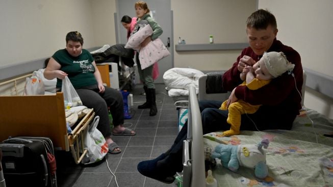 Orang tua dan anak-anak mereka yang merupakan pasien rumah sakit anak pusat Kyiv mengumpulkan barang-barang sebelum dievakuasi ke Polandia dan Jerman di Kyiv, Ukraina, Sabtu (5/3/2022). [Sergei SUPINSKY / AFP]
