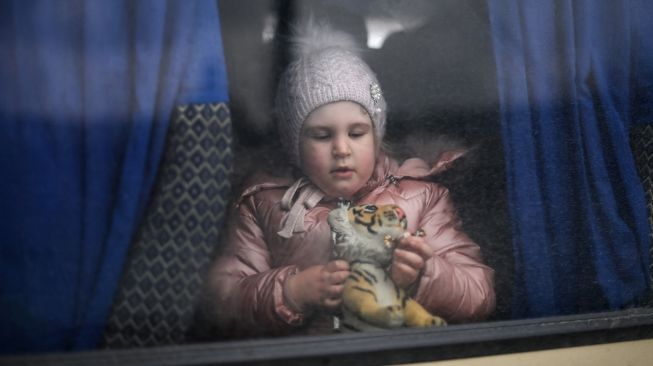 Seorang gadis bermain dengan mainan saat dia menunggu di dalam bus mini menuju kota Uzhhorod di dekat perbatasan dengan Slovakia di stasiun kereta Lviv, Ukraina barat, Sabtu (5/3/2022). [Daniel LEAL / AFP]