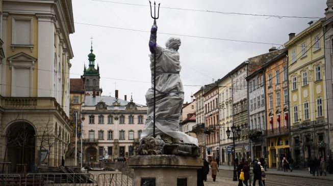 Warga berjalan melewati patung-patung bersejarah yang dibungkus di Archcathedral Basilica of the Assumption of the Blessed Virgin Mary atau Katedral Latin di Lviv, Ukraina, Sabtu (5/3/2022). [Daniel LEAL / AFP]