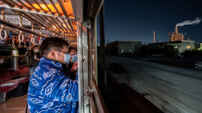 Penumpang melihat pemandangan saat menaiki kereta yang populer untuk tur wisata malam hari yang melintasi jalur kereta Gakunan melalui kawasan industri di Fuji, prefektur Shizuoka, Jepang, Sabtu (26/2/2022). [Philip FONG / AFP]