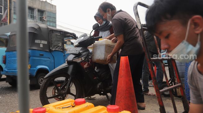 Pedagang menaikkan jerigen berisi minyak goreng curah ke atas motor di Pasar Kebayoran Lama, Jakarta, Rabu (9/3/2022). [Suara.com/Angga Budhiyanto] 