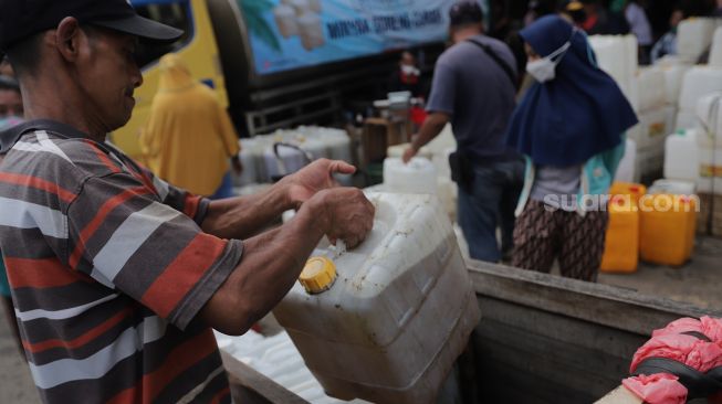 Pedagang membawa jerigen berisi minyak curah saat distribusi minyak goreng curah di Pasar Kebayoran Lama, Jakarta, Rabu (9/3/2022). [Suara.com/Angga Budhiyanto] 