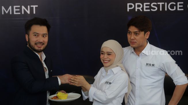 Presiden Direktur Prestige Motorcars Rudy Salim (kiri) menerima potongan tumpeng dari Pendiri Leslar Entertainment Lesti Kejora (tengah) usai menandatangani akuisisi Leslar Entertainment oleh Prestige Corp di Prestige Image Corp, Pluit, Jakarta, Jumat (11/3/2022). [Suara.com/Angga Budhiyanto]