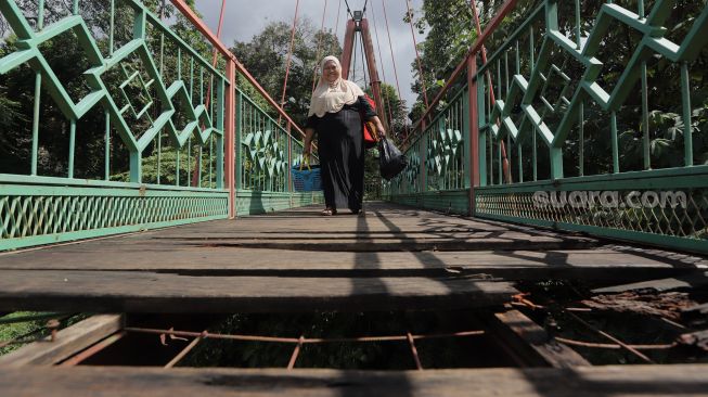 Warga berjalan melintasi Jembatan Wiratman, Kelurahan Srengseng Sawah, Jakarta, Sabtu (12/3/2022). [Suara.com/Angga Budhiyanto]