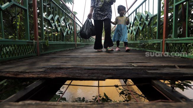 Warga berjalan melintasi Jembatan Wiratman, Kelurahan Srengseng Sawah, Jakarta, Sabtu (12/3/2022). [Suara.com/Angga Budhiyanto]