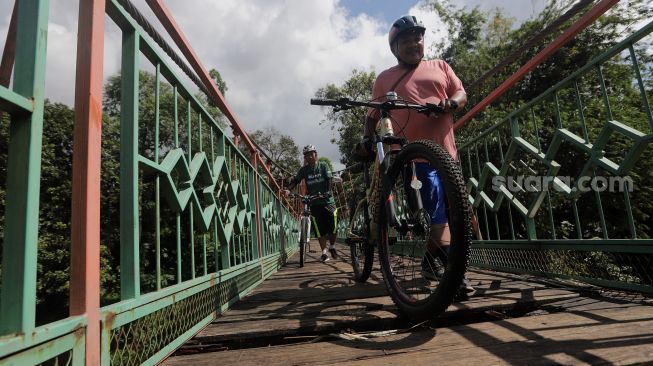 Warga membawa sepedanya berjalan melintasi Jembatan Wiratman, Kelurahan Srengseng Sawah, Jakarta, Sabtu (12/3/2022). [Suara.com/Angga Budhiyanto]