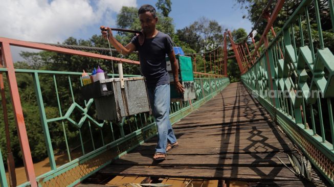 Seorang pedagang berjalan melintasi Jembatan Wiratman, Kelurahan Srengseng Sawah, Jakarta, Sabtu (12/3/2022). [Suara.com/Angga Budhiyanto]