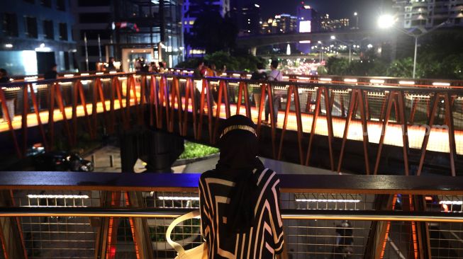 Warga berdiri di Jembatan Penyeberangan Orang (JPO) Pinisi Karet-Sudirman, Jakarta, Sabtu (12/3/2022). [Suara.com/Angga Budhiyanto]