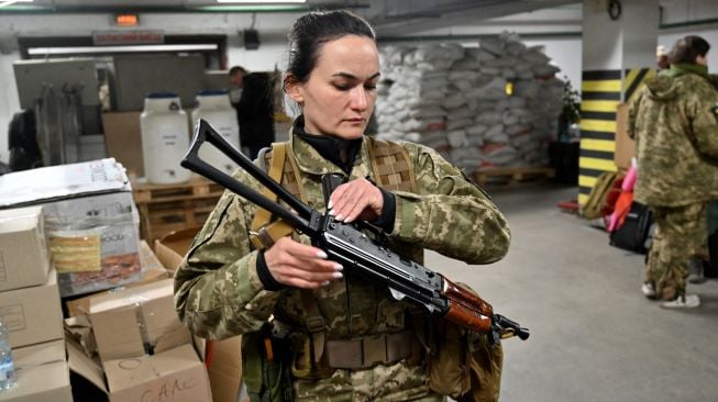 Iryna Sergeyeva, salah satu prajurit relawan wanita pertama yang mendapatkan kontrak militer penuh dari Pasukan Pertahanan Teritorial Ukraina, memegang senapan mesin Kalashnikov saat dia menghadiri pelatihan militer di garasi bawah tanah yangtelah diubah menjadi pangkalan pelatihan dan logistik di Kyiv, Ukraina, Jumat (11/3/2022). [Sergei SUPINSKY / AFP]