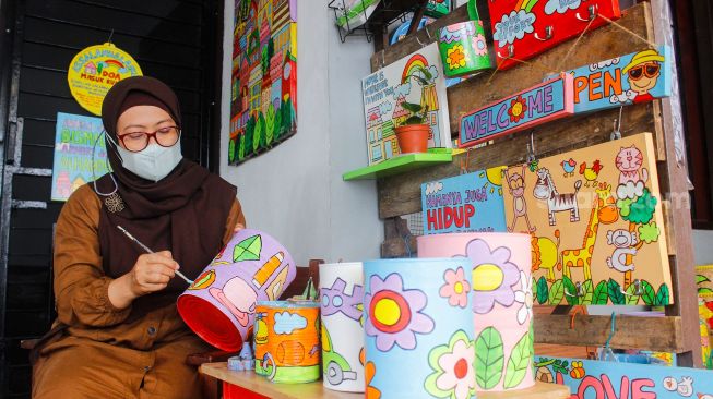 Lani Cahyaningsari (48) menyelesaikan pembuatan kerajinan lukis di atas media kaleng bekas di Kaleng Lani, Depok, Jawa Barat, Minggu (13/3/2022). [Suara.com/Septian]