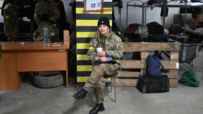 Seorang prajurit wanita Pasukan Pertahanan Teritorial Ukraina, minum teh di garasi bawah tanah yang telah diubah menjadi pangkalan pelatihan dan logistik di Kyiv, Ukraina, Jumat (11/3/2022). [Sergei SUPINSKY / AFP]