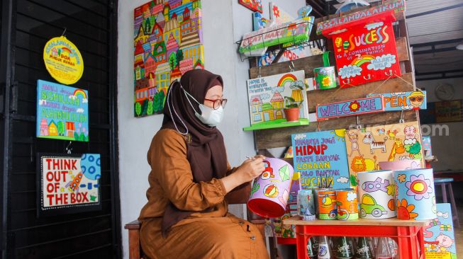 Lani Cahyaningsari (48) menyelesaikan pembuatan kerajinan lukis di atas media kaleng bekas di Kaleng Lani, Depok, Jawa Barat, Minggu (13/3/2022). [Suara.com/Septian]