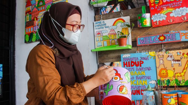 Lani Cahyaningsari (48) menyelesaikan pembuatan kerajinan lukis di atas media kaleng bekas di Kaleng Lani, Depok, Jawa Barat, Minggu (13/3/2022). [Suara.com/Septian]